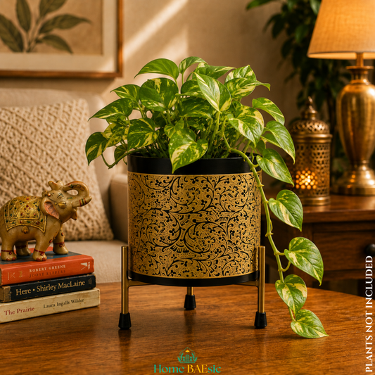 Black and gold Vines metal planter with a lush trailing pothos plant on a sturdy gold metal stand, styled as an elegant home décor accent in a warm living room.