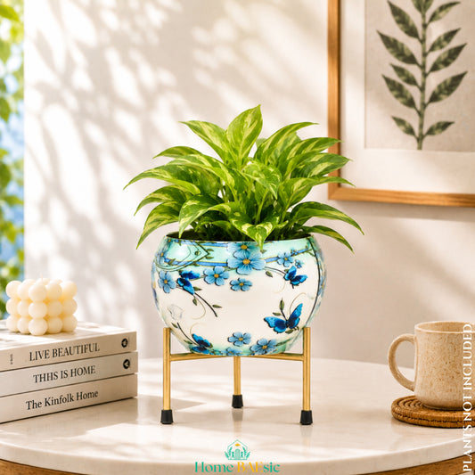 Blue Butterfly Floral metal planter with golden metal stand and green indoor plant styled on a wooden table with books in a warm home décor setting