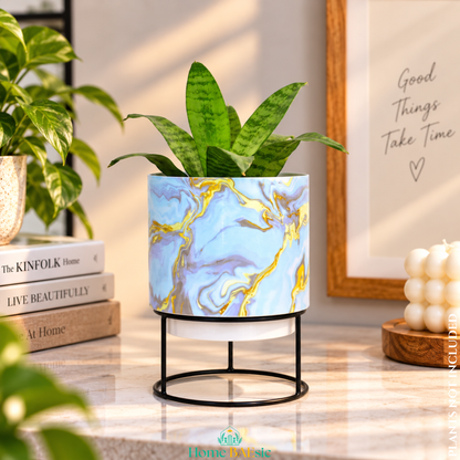 Blue & Gold Marble designer metal tumbler planter with stand, featuring elegant blue, turquoise, white and gold marble artwork with a green indoor plant, styled as a sophisticated home decor accent.