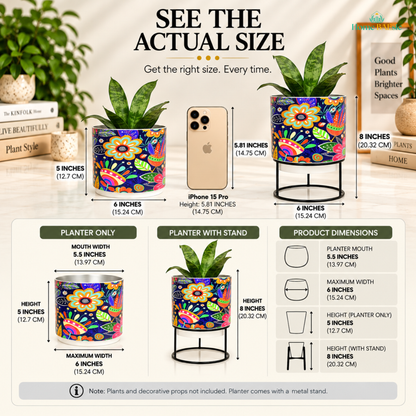 Home BAEsic Floral Doodle Tumbler Metal Planter size guide showing the colorful floral-patterned metal planter with and without its black metal stand, compared with an iPhone 15 Pro for scale. The infographic highlights a 5.5-inch mouth width, 6-inch maximum width, 5-inch planter height, and 8-inch height with stand, with detailed product dimension callouts. Plants and decorative props are not included; the planter comes with a metal stand.