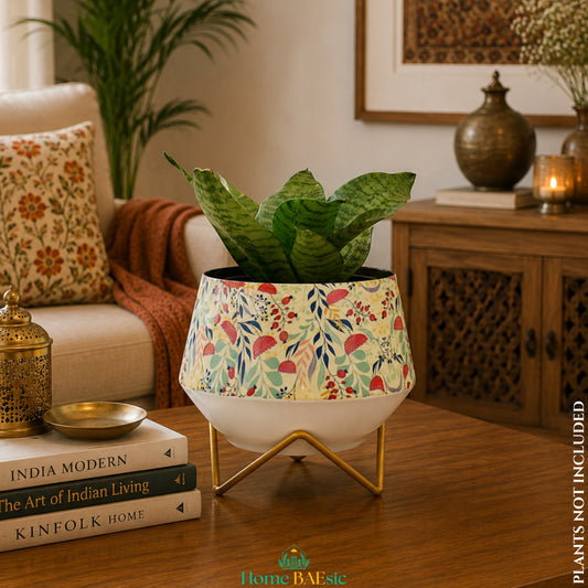 Garnet floral metal planter with a green indoor plant on a gold metal stand, styled with books in a warm home setting.