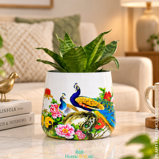 A Peacocks in Garden tumbler planter featuring decorative peacock and floral illustration and green indoor snake plant, set on a marble table in a cozy living room.