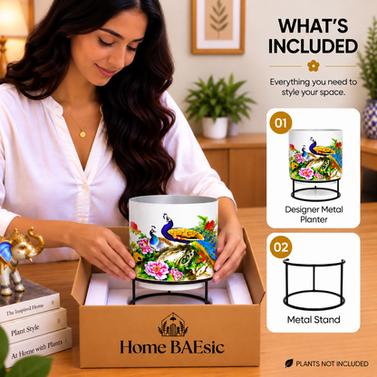 Home BAEsic Peacocks in Garden designer metal tumbler planter with black metal stand, shown in a lifestyle unboxing scene with a woman holding the empty planter above its branded packaging box; a “What’s Included” panel highlights the planter and stand, with plants not included.