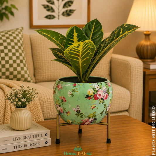 Sea green floral metal planter with colorful flower pattern on a golden stand, styled with an indoor plant in a cozy living room setting.