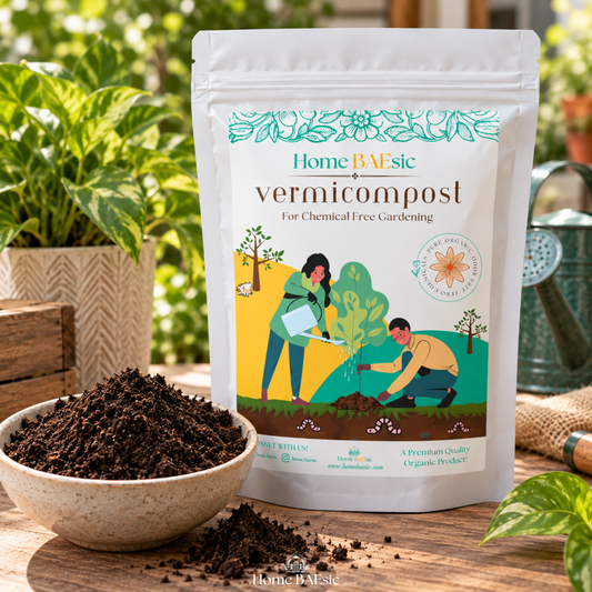 A stand-up pouch of HomeBAsic Vermicompost for chemical free gardening, displayed on a wooden table next to a bowl of compost. The background features a blurred garden setting with a potted plant and a watering can.