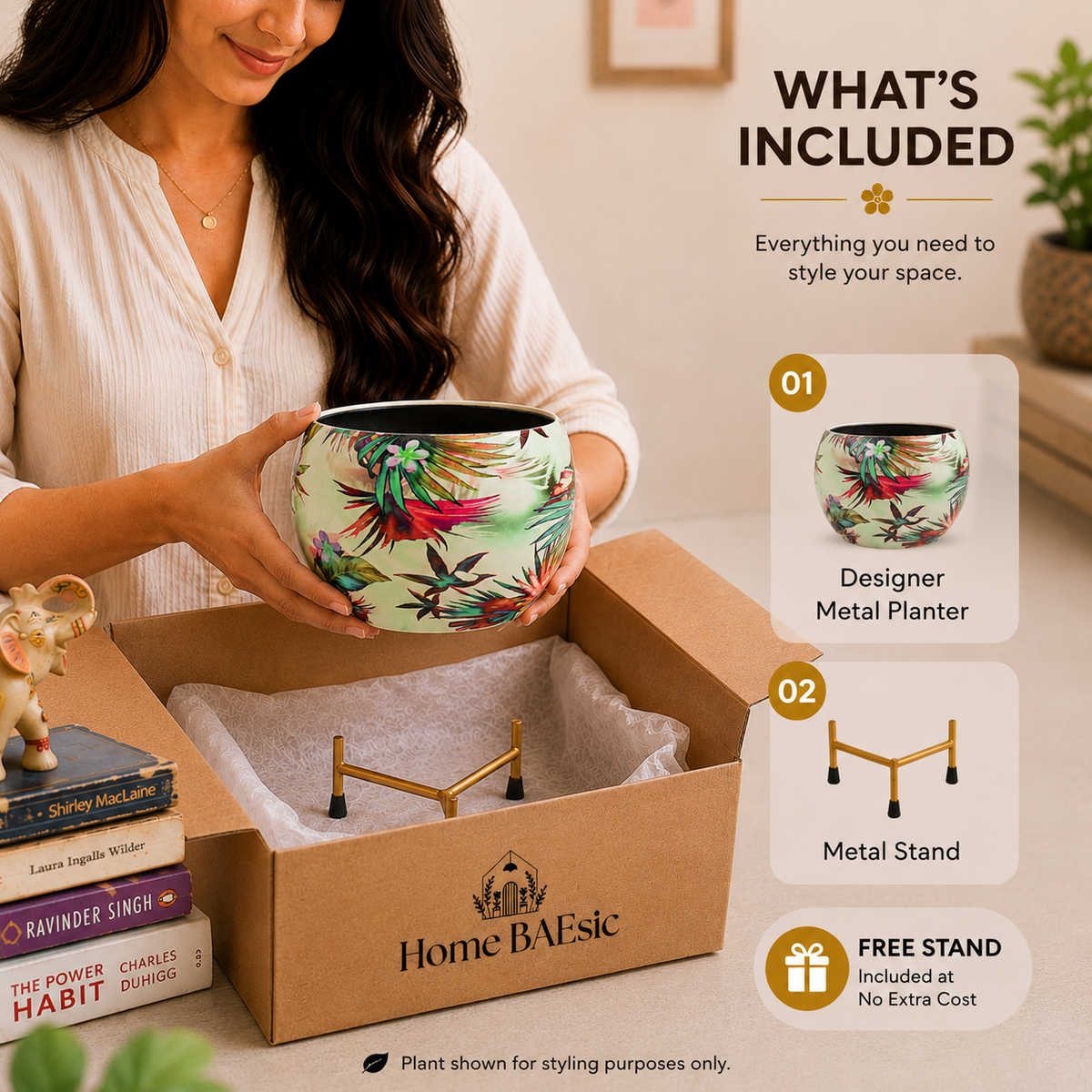 A woman holds a decorative metal planter above an open cardboard box labeled Home BAEsic, with included items listed on the right: a designer metal planter, a metal stand, and a free stand. The planter has a light green base with a colorful tropical floral print.