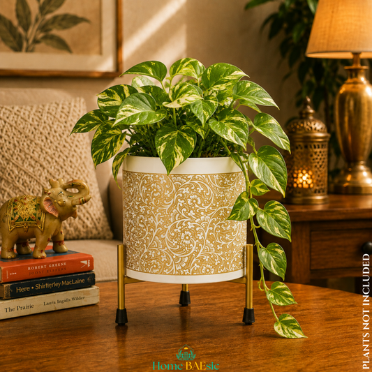 White Golden Vines designer metal planter with gold floral pattern and matching metal stand, styled with a lush trailing pothos plant in a warm, elegant living room